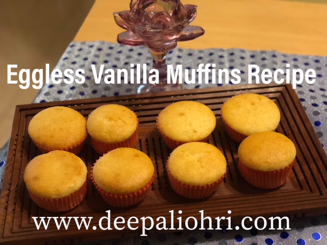 Eight eggless vanilla muffins in paper liners on a wooden tray