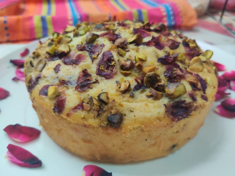Eggless thandai pistachio rose cake topped with pistachios and rose petals