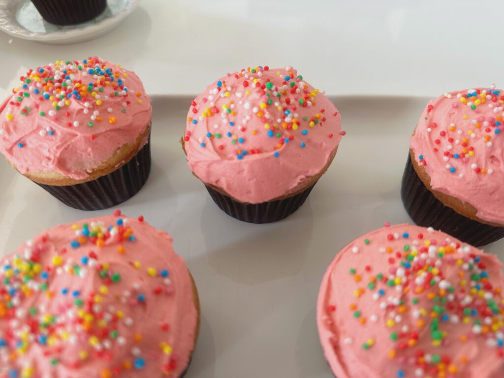 Freshly baked vanilla cupcakes with buttercream frosting, topped with colorful sprinkles.