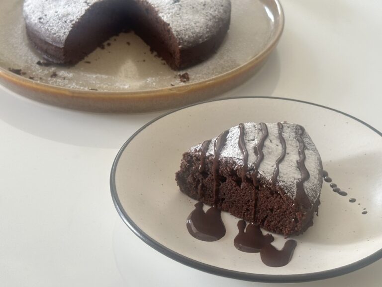 🍫 Gâteau Au Chocolat — The Classic French Chocolate Cake Recipe Close-up of a rich, moist French chocolate cake (Gâteau au Chocolat) topped with fresh raspberries and powdered sugar, placed on a white plate.
