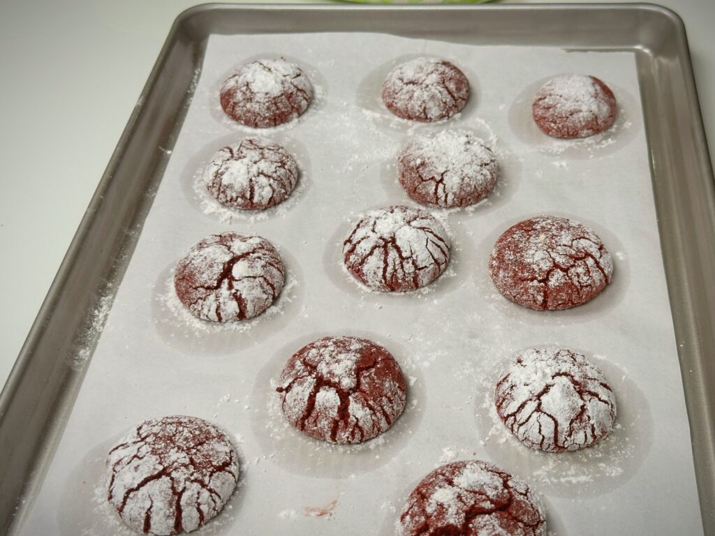 Freshly baked red velvet crinkle cookies dusted with powdered sugar on a parchment-lined baking tray.