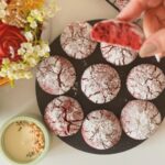 Red velvet crinkle cookies dusted with powdered sugar on a black plate, with one cookie broken open to show the soft fudgy center.
