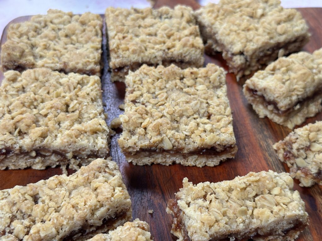 Soft and buttery strawberry jam bars cut into squares, showing a thick fruity jam layer between a tender cookie base and golden oat crumble topping, arranged on a wooden board.