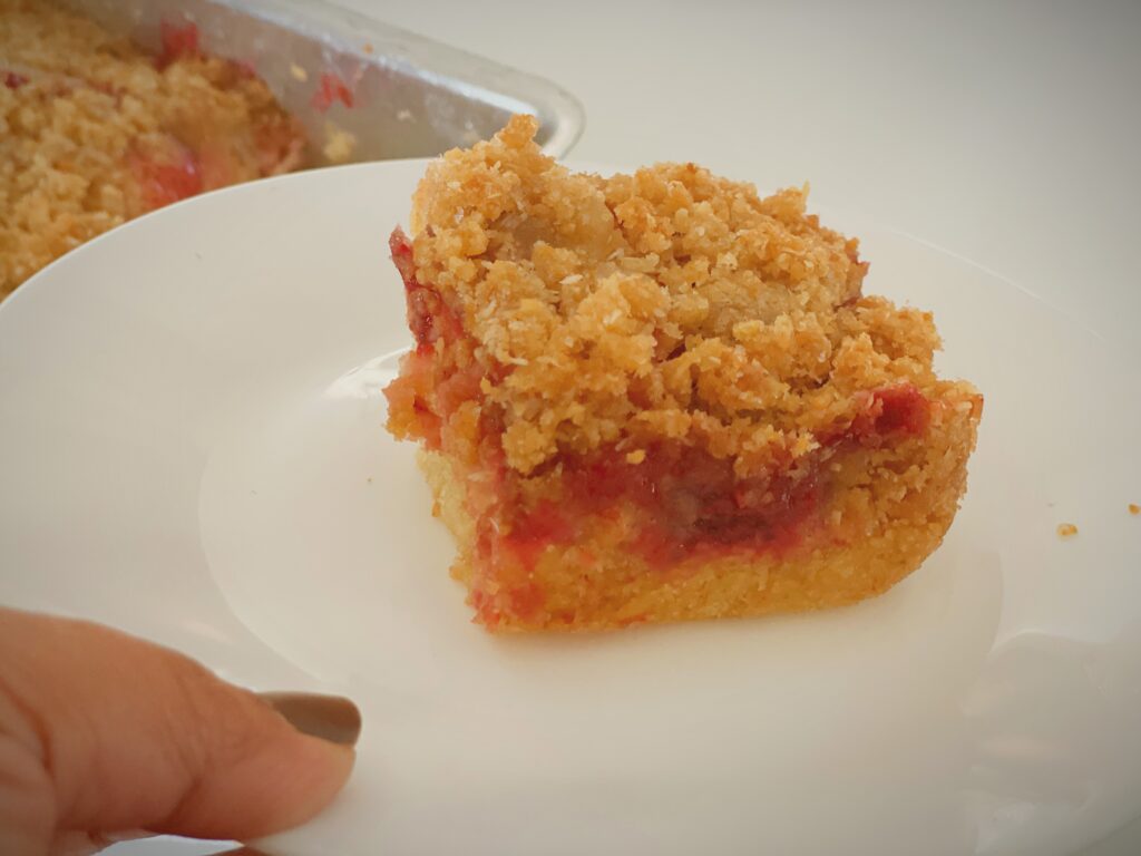 Close-up slice of strawberry streusel cake on a white plate showing soft cake, strawberry filling, and crumb topping.