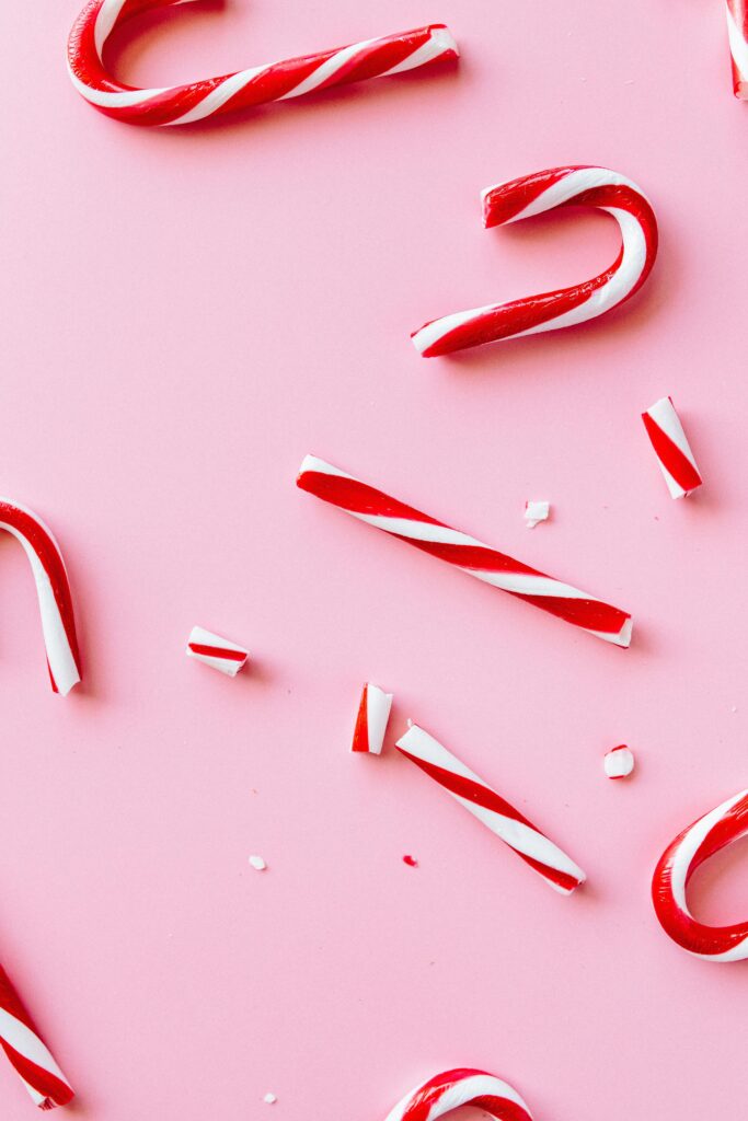 Crushed red and white candy canes scattered on a pink background, showing broken pieces and striped candy texture.