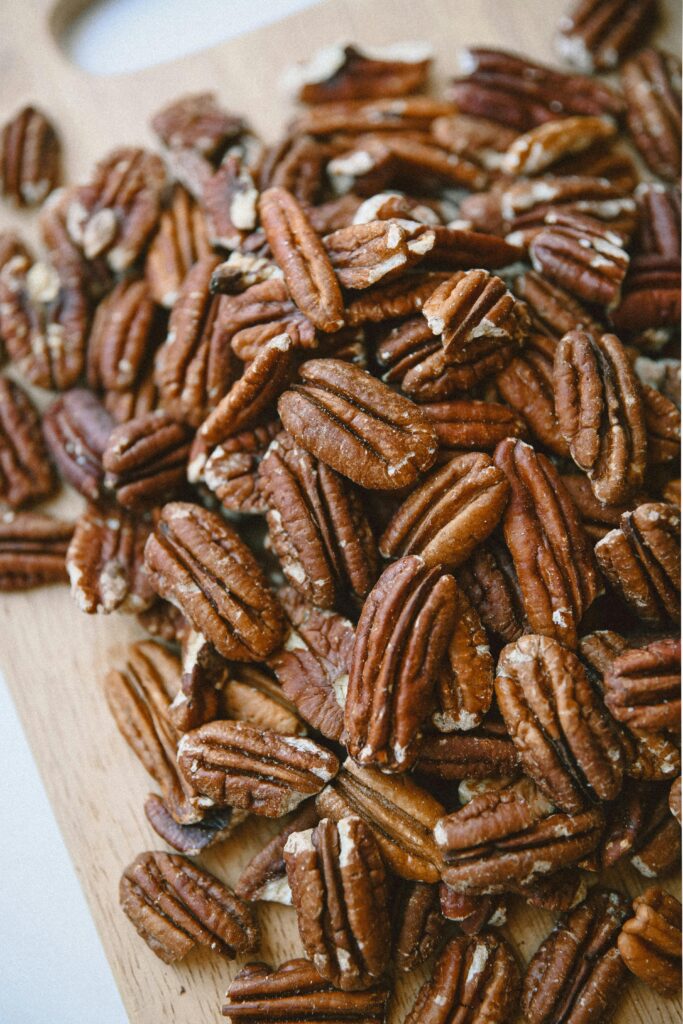 Close-up of toasted pecan halves spread on a wooden cutting board, showing their rich brown color and natural texture.