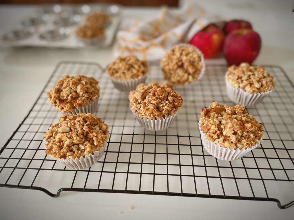 Eggless apple crumble muffins with oat walnut streusel topping cooling on wire rack with fresh apples in background