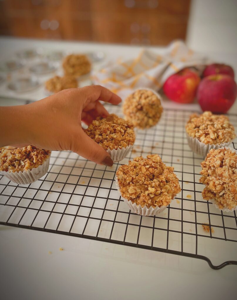 Hand picking up eggless apple crumble muffin with crunchy streusel topping from cooling rack