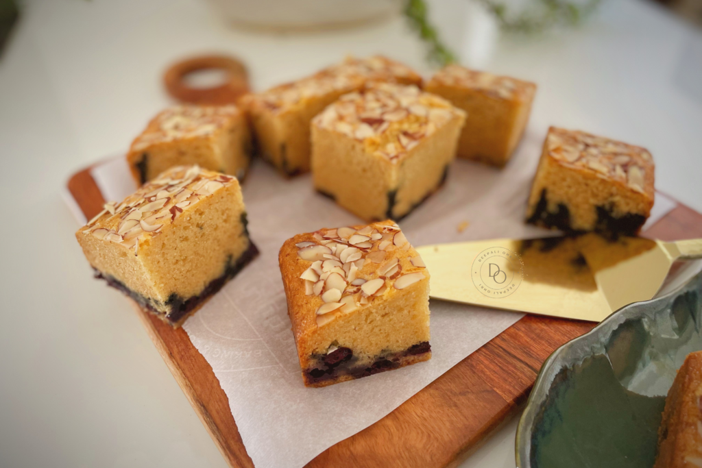 Eggless blueberry almond cake squares topped with sliced almonds arranged on parchment over a wooden board