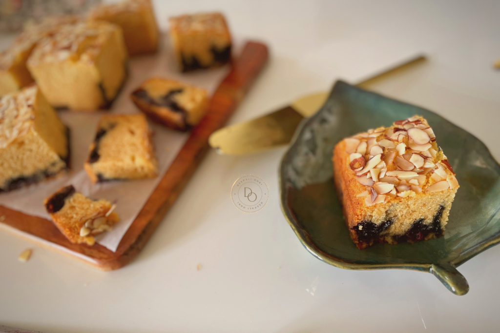 Slice of eggless blueberry almond cake topped with sliced almonds served on a green leaf-shaped plate