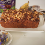 Banana streusel bread topped with walnuts, caramel toffees and chocolate chunks on a white plate