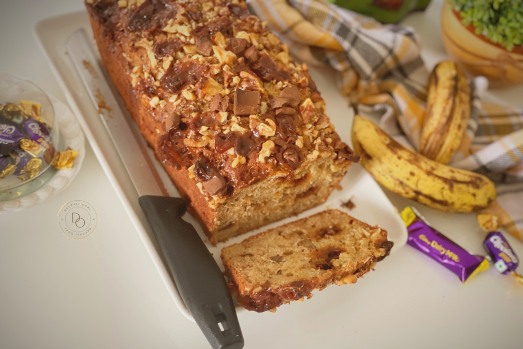 Banana streusel bread loaf topped with walnuts, caramel toffees and chocolate chunks with a sliced piece showing the moist crumb