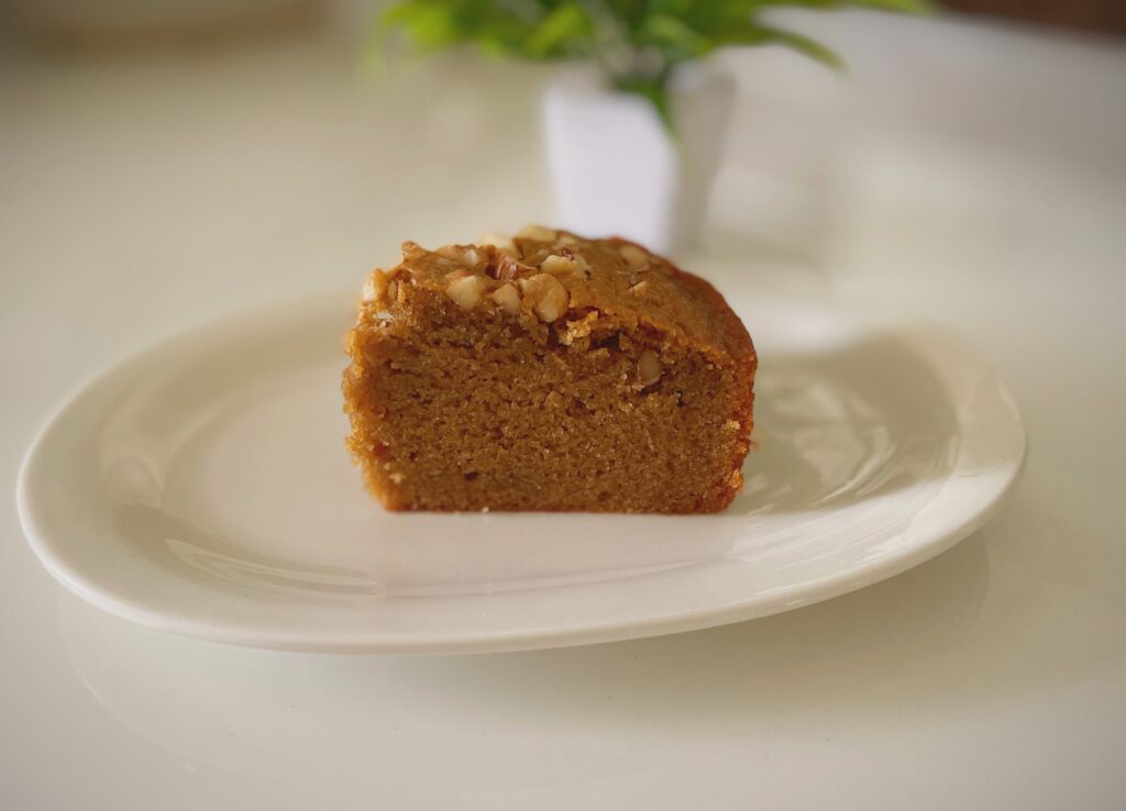 A slice of eggless coffee walnut cake on a white plate showing soft moist crumb and toasted walnuts on top