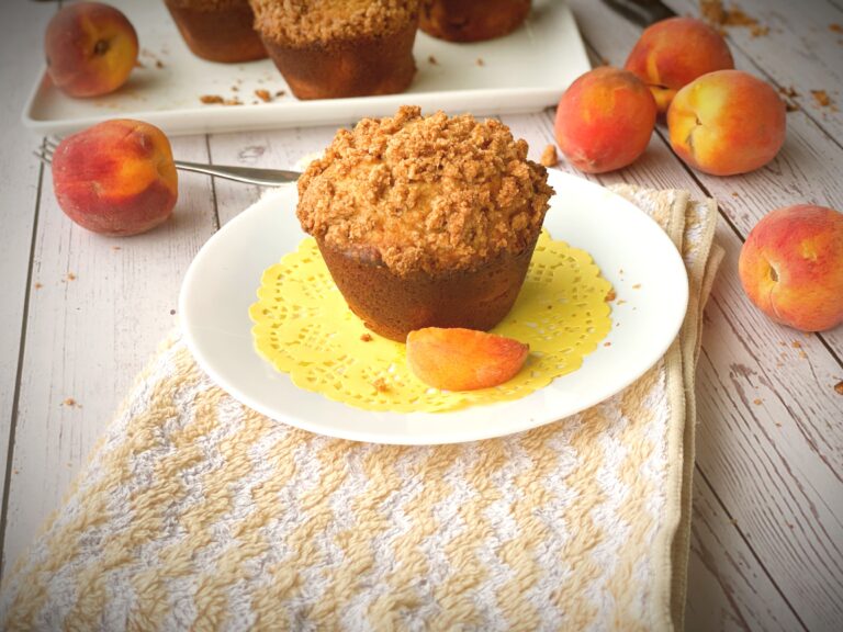 Brown butter peach cobbler muffin with golden streusel topping on a yellow doily with fresh peaches