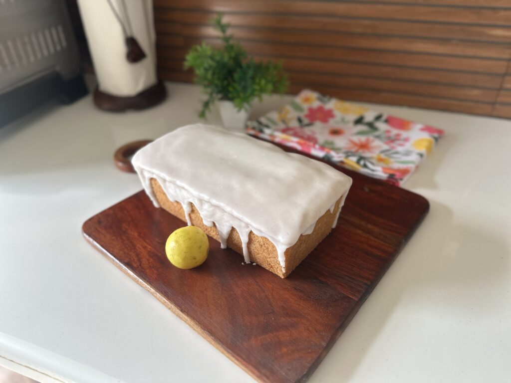 Mary Berry lemon drizzle cake with white icing glaze on a wooden board, topped with fresh lemon