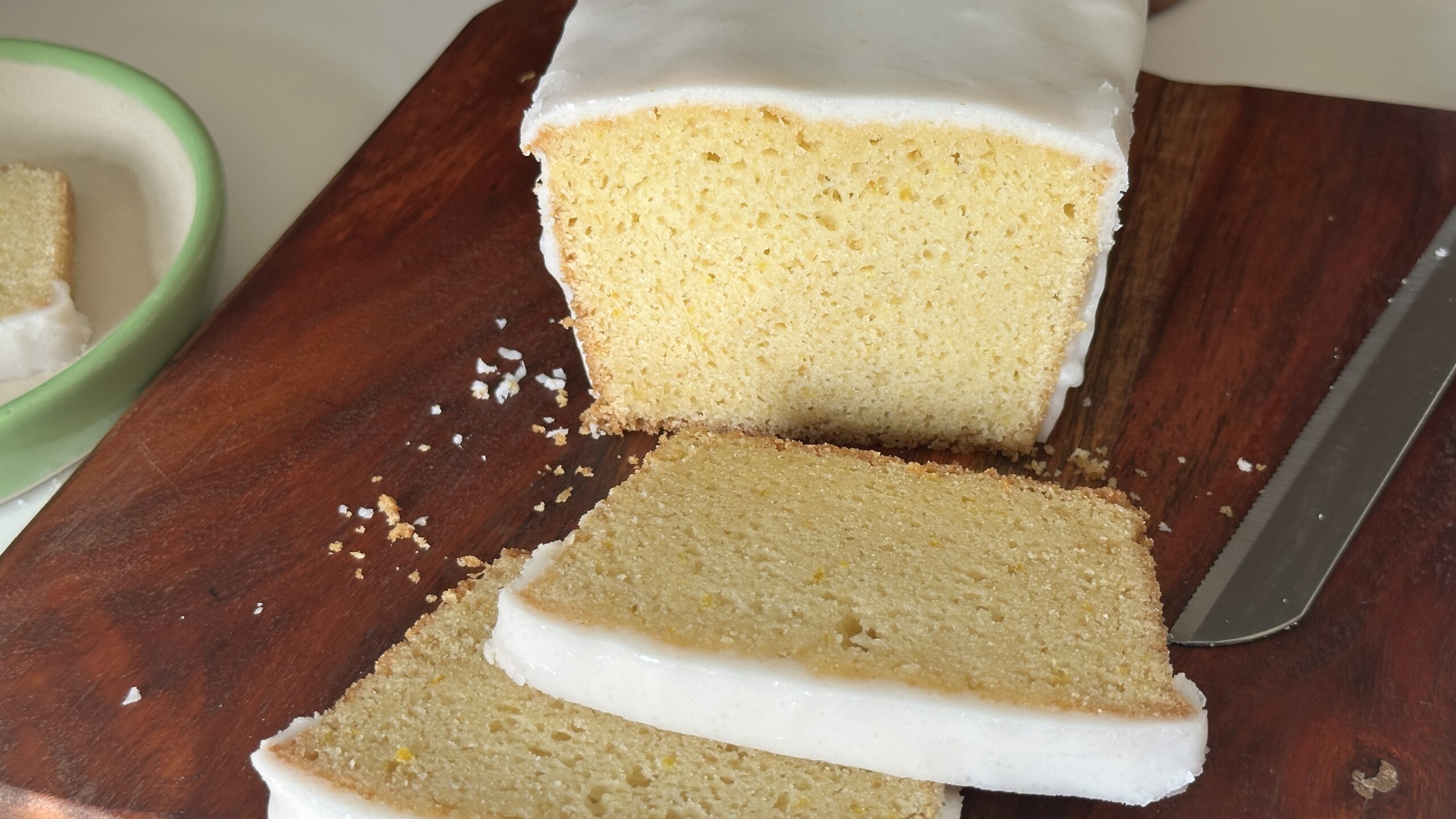 Mary Berry lemon drizzle cake sliced on wooden board showing moist crumb with icing glaze and knife