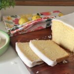 Moist Mary Berry inspired lemon drizzle cake with white icing glaze, sliced on a wooden board with fresh lemons in the background