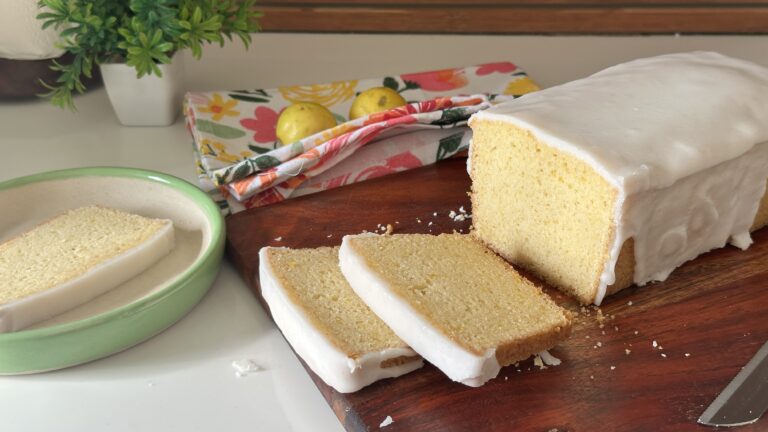 Moist Mary Berry inspired lemon drizzle cake with white icing glaze, sliced on a wooden board with fresh lemons in the background