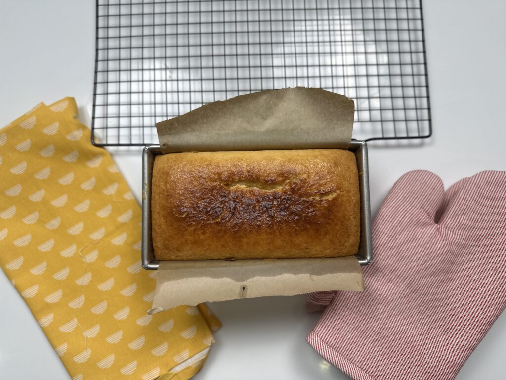 Freshly baked condensed milk cake in a loaf tin lined with parchment paper, golden brown on top, just out of the oven