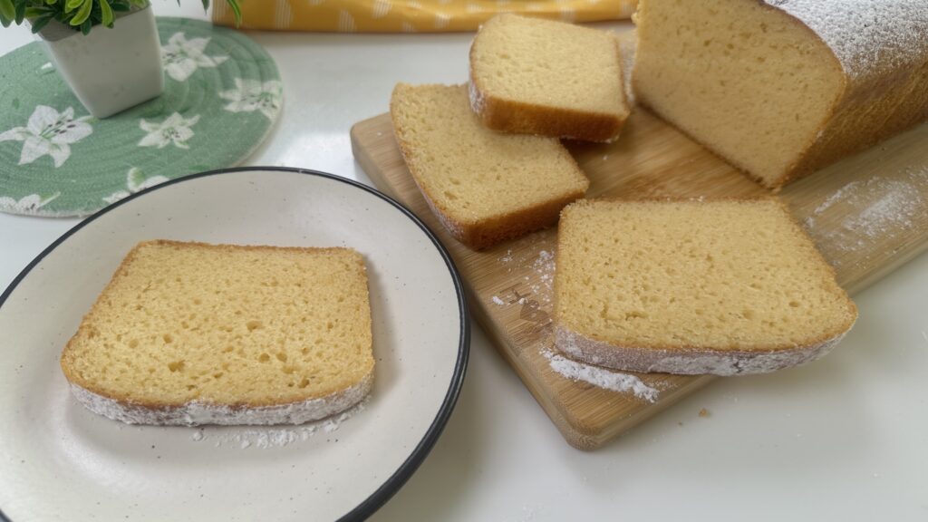 Soft and moist condensed milk cake sliced on a wooden board with powdered sugar, one slice on a white plate