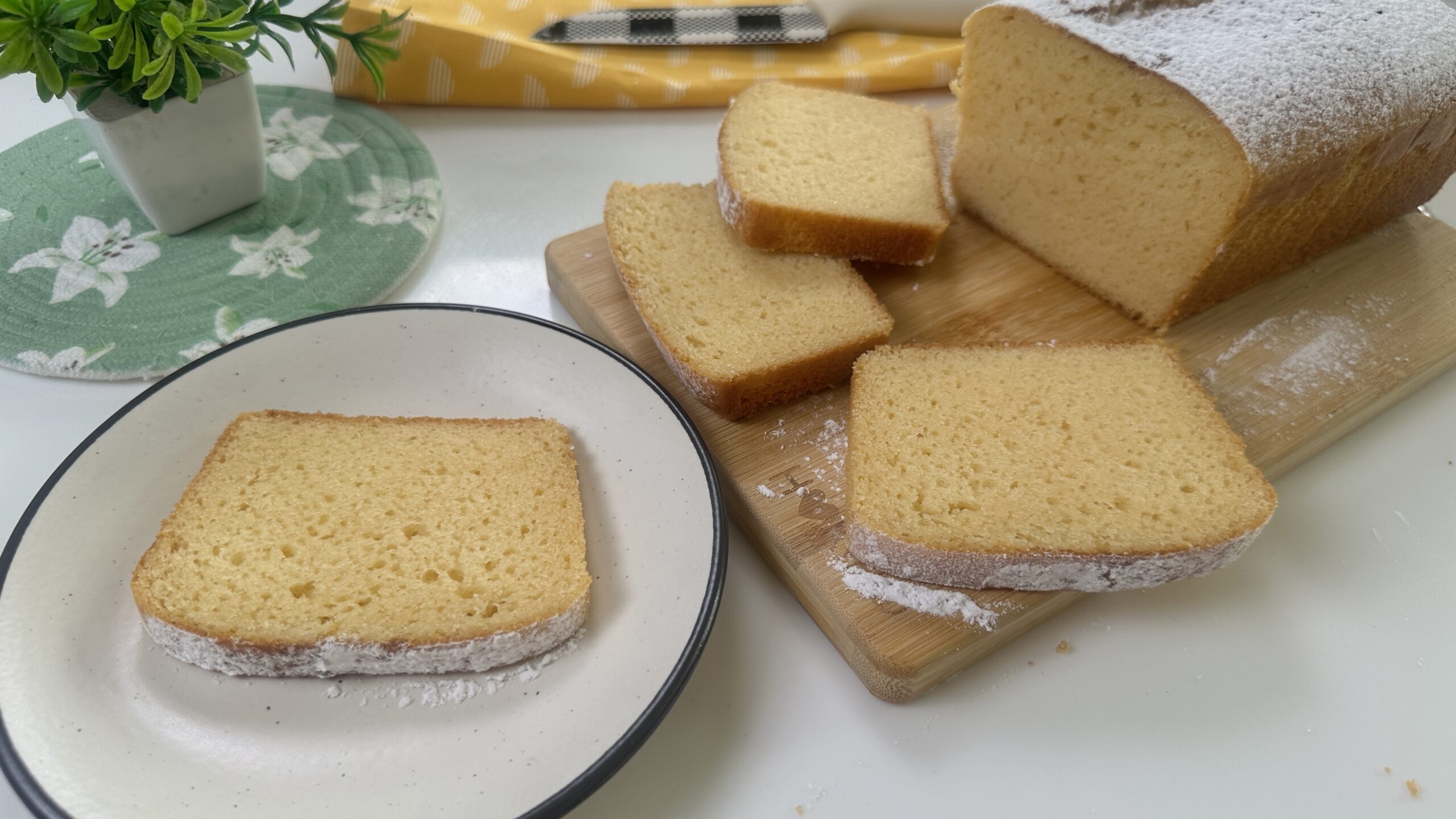 Sliced condensed milk cake on a wooden board with powdered sugar and one slice on a white plate