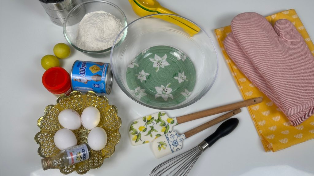 Ingredients for condensed milk cake including eggs, Milkmaid condensed milk, flour, butter and lemon on a white surface