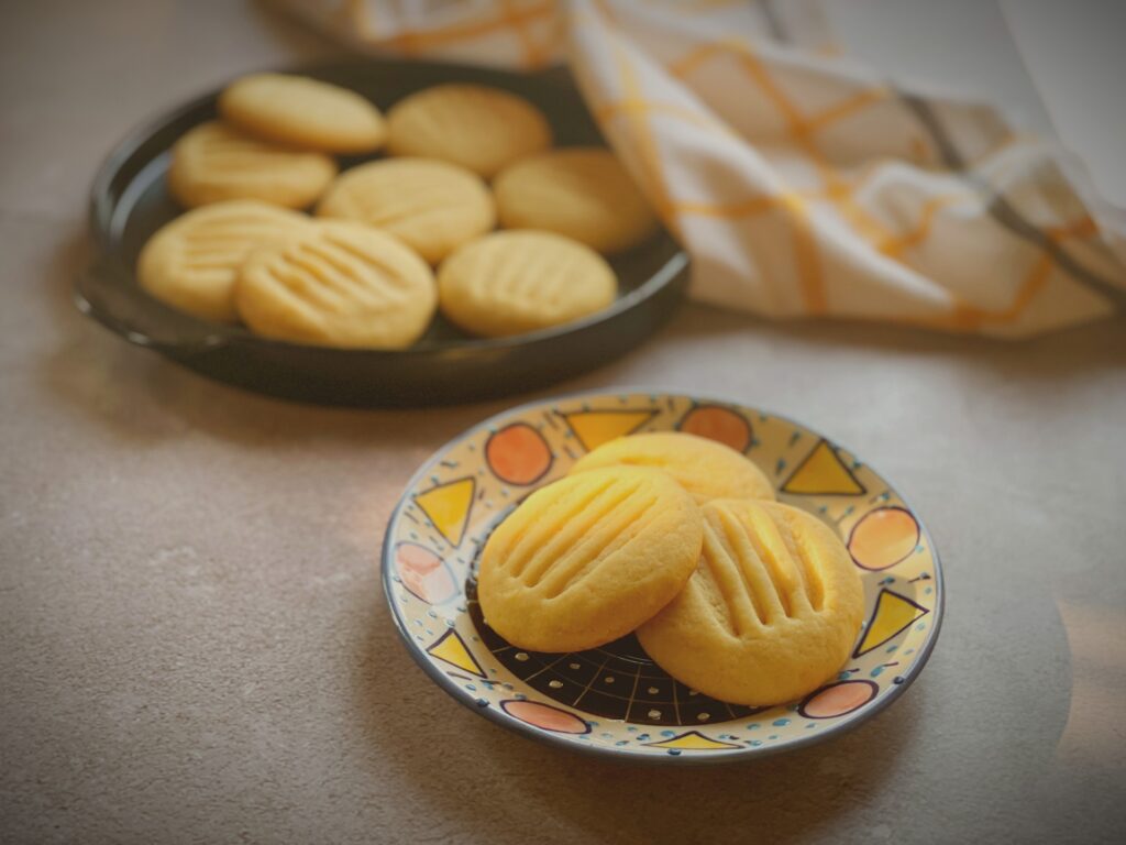 Close-up of eggless condensed milk cookies showing fork-pressed pattern and golden crisp edges on a decorative geometric plate