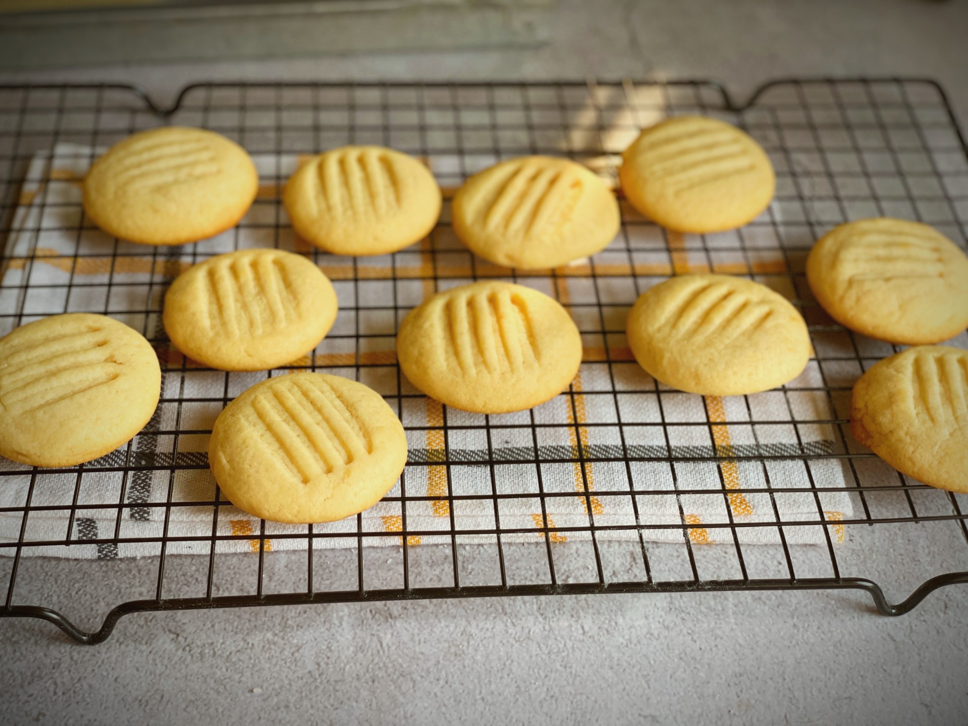 Twelve golden eggless condensed milk cookies on a wire cooling rack with fork-pressed crisscross pattern