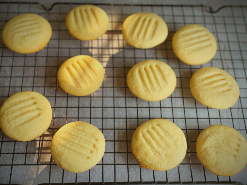 Twelve freshly baked eggless condensed milk cookies arranged on a wire cooling rack