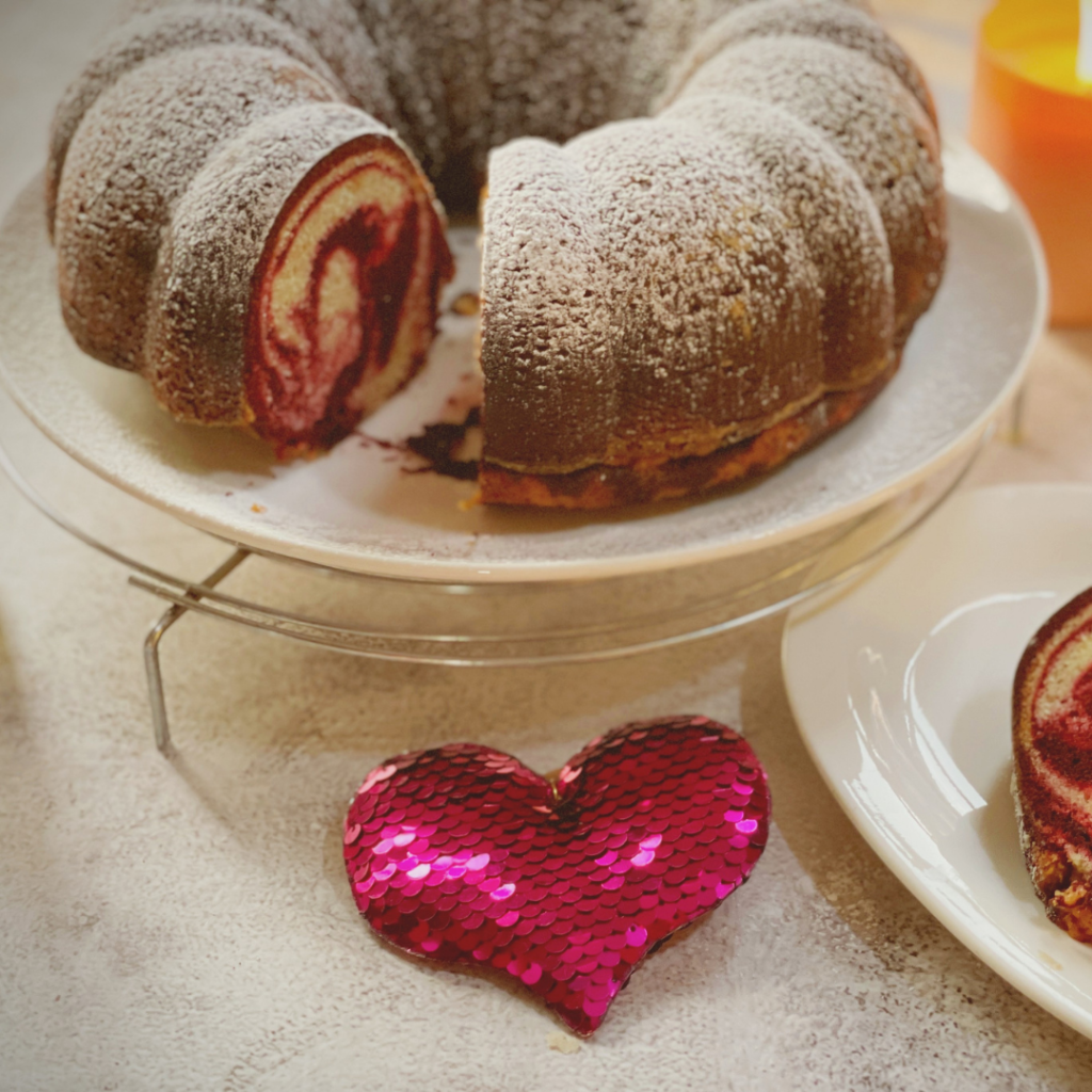 Sliced red velvet marble cake on a cake stand with a sequin heart decoration beside it, styled for Valentine's Day