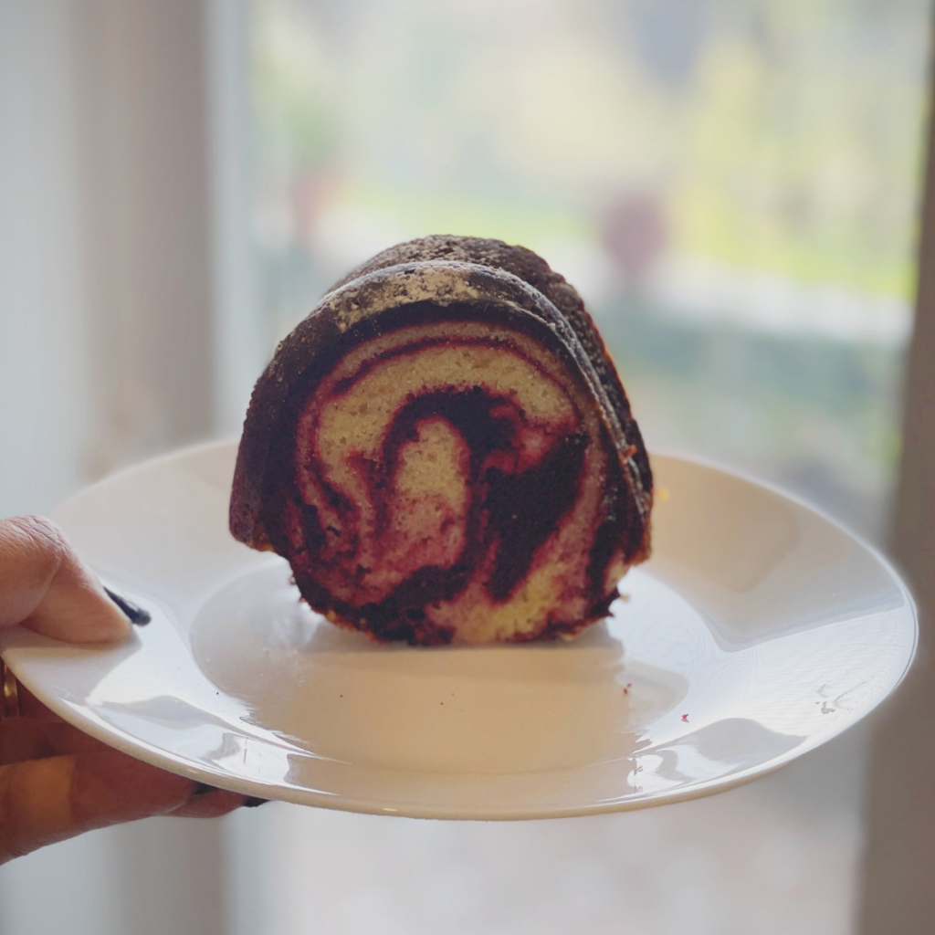 Hand holding a white plate with a single slice of red velvet marble cake showing the swirl pattern