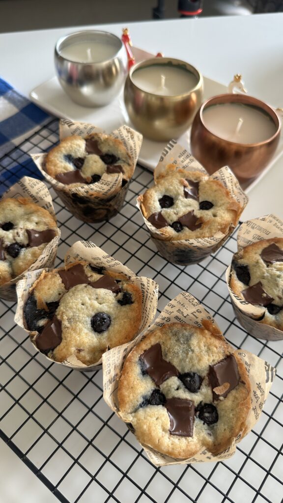 Six freshly baked Blueberry Chocolate Muffins on a wire cooling rack with candles in the background