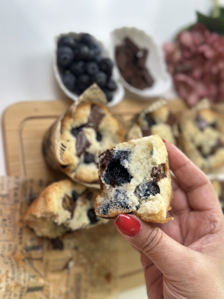 Hand holding a Blueberry Chocolate Muffin broken open showing soft interior with blueberries and melted chocolate