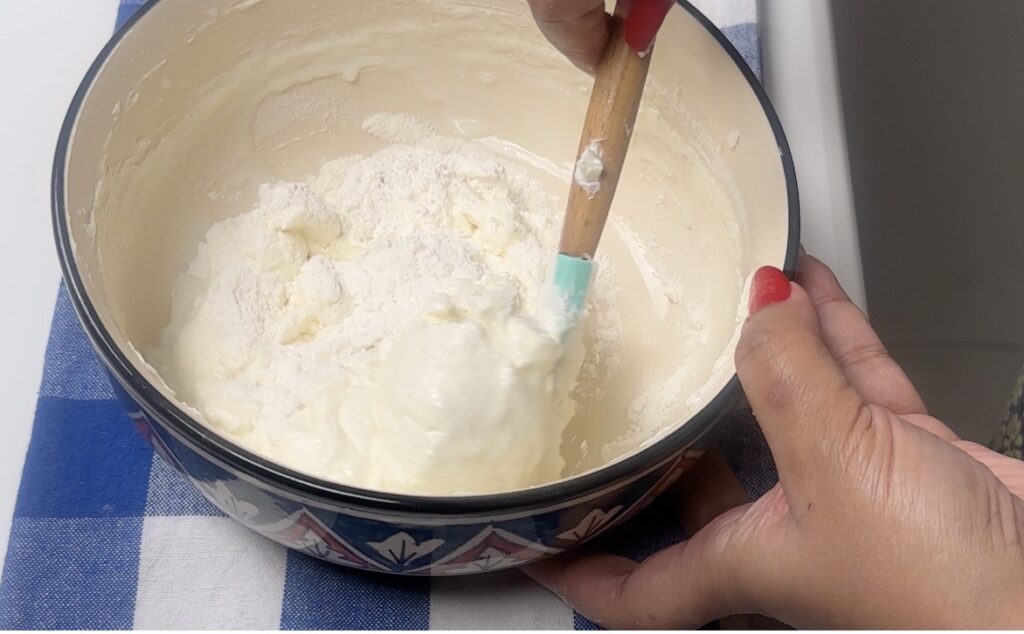 Hands folding flour into muffin batter with a spatula — gentle folding technique shown