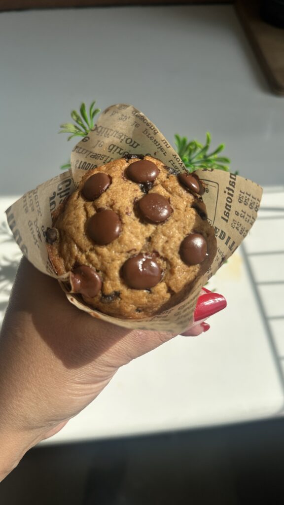 eggless banana chocolate chip muffin in newspaper tulip liner on a wooden board