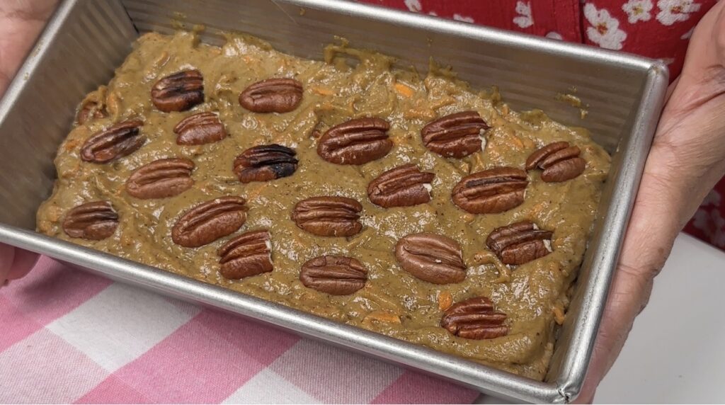 Eggless date and carrot cake batter in a loaf pan, topped with whole pecans before baking