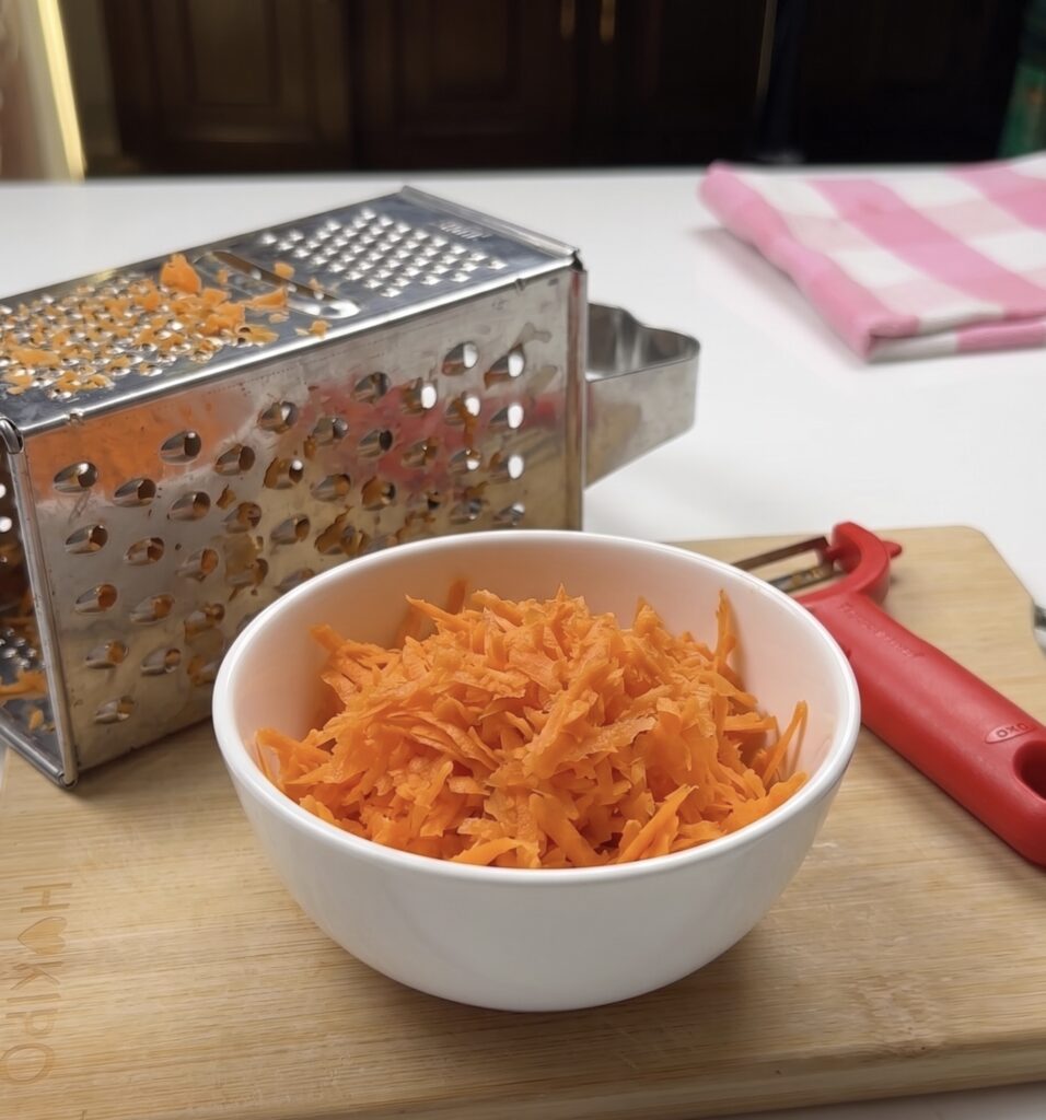 Freshly grated carrots in a white bowl for an eggless loaf cake