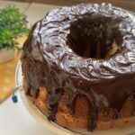 Large vanilla bundt cake with glossy chocolate glaze dripping down the sides on a wire rack