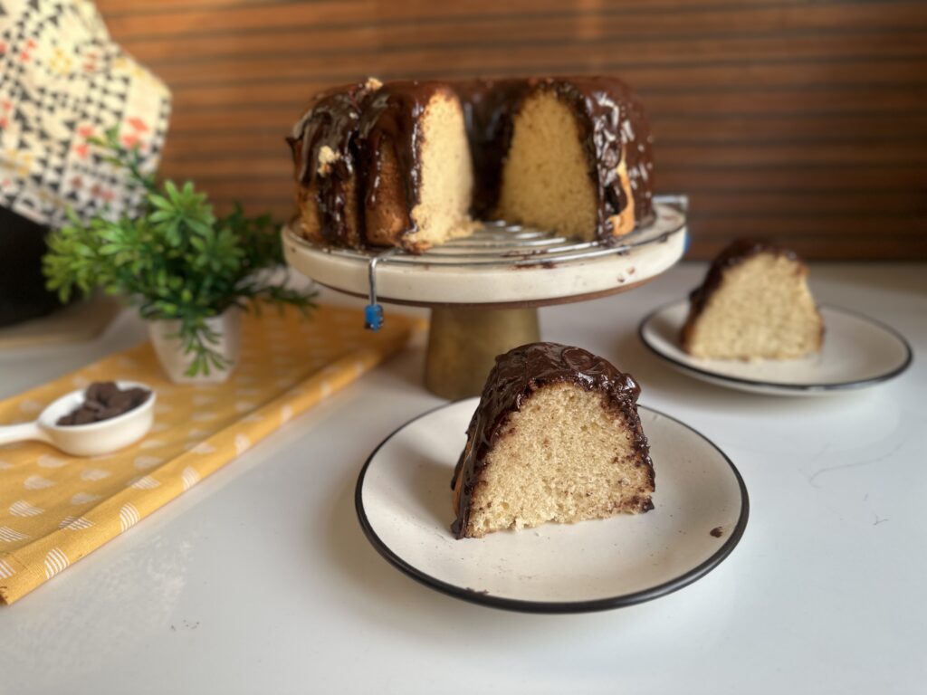 Slice of vanilla bundt cake with chocolate glaze on a plate beside the whole cake