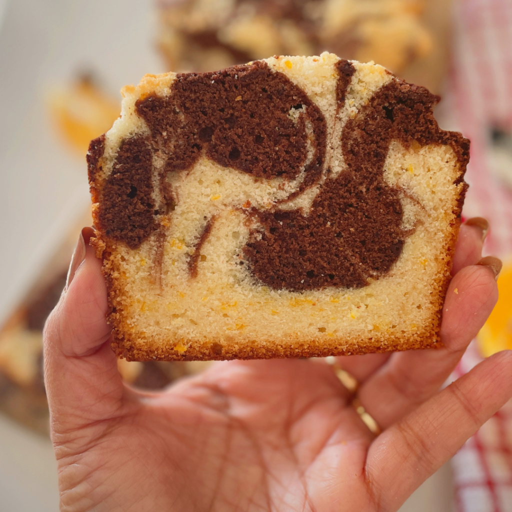 Hand holding a slice of chocolate orange marble cake