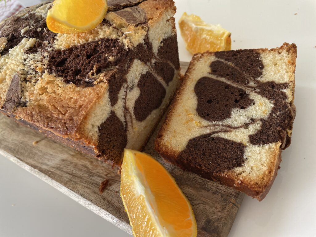 Chocolate orange marble cake loaf on rustic board with orange wedges and checkered napkin