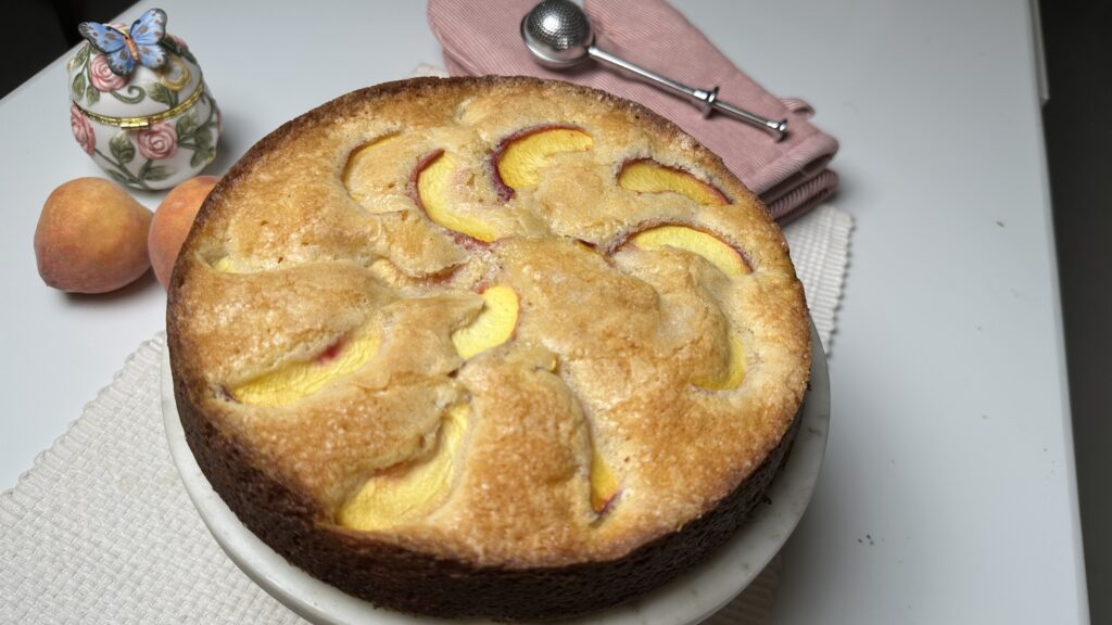 Uncut peach butter cake dusted with powdered sugar on a marble stand