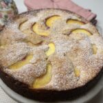 Angled shot of whole peach butter cake dusted with powdered sugar on a marble stand