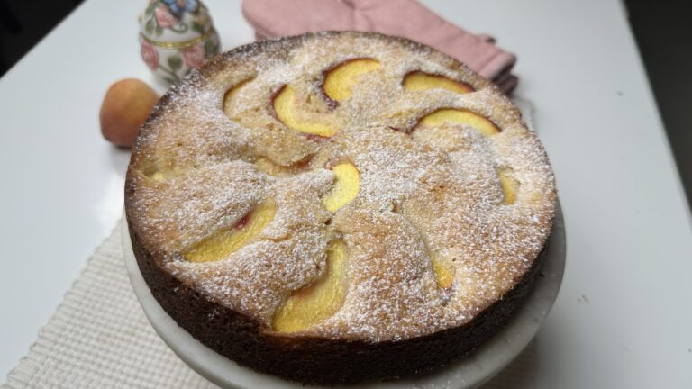 Peach Butter Cake Angled shot of whole peach butter cake dusted with powdered sugar on a marble stand