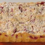 Whole plum streusel cake dusted with powdered sugar on parchment paper and a wooden board