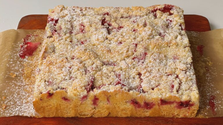 Whole plum streusel cake dusted with powdered sugar on parchment paper and a wooden board
