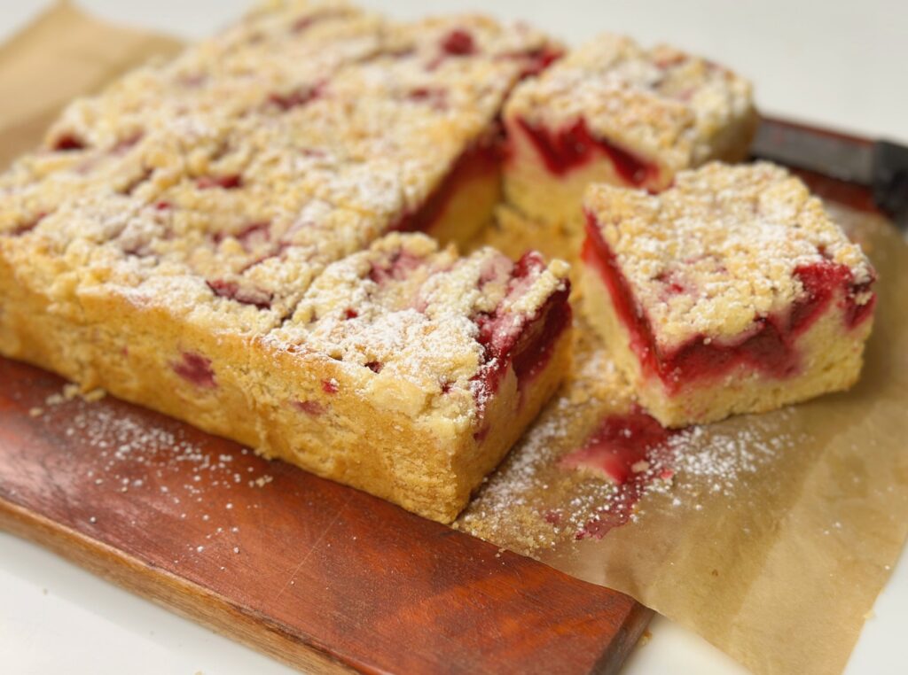 Plum streusel cake cut into squares on a wooden board with a knife alongside