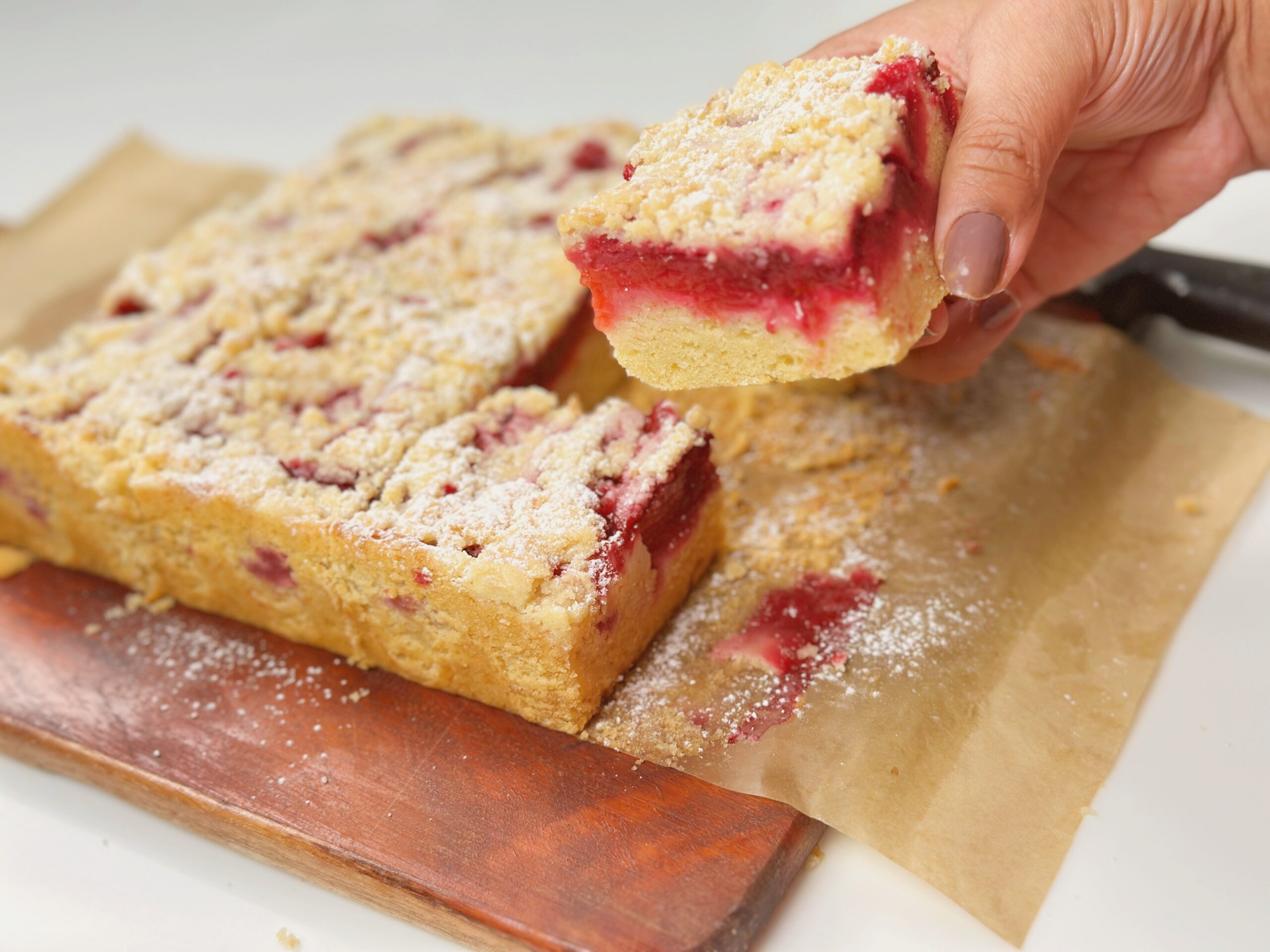 Hand holding a slice of plum streusel cake showing the jammy plum layer between cake and streusel