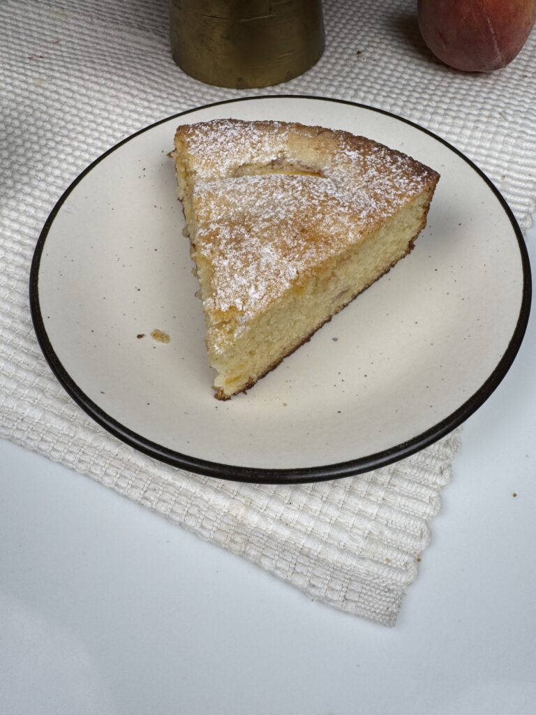 Close-up of a single slice of peach butter cake dusted with powdered sugar on a plate