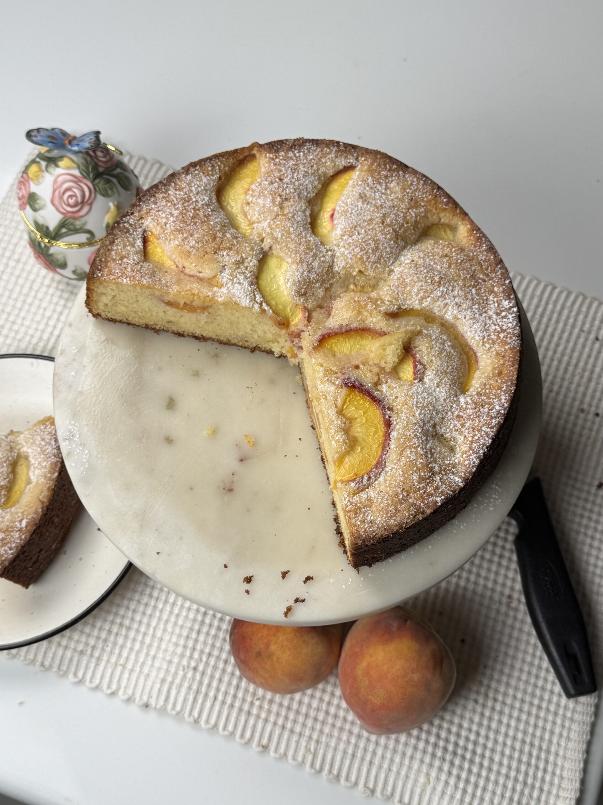 Overhead view of peach butter cake on a marble stand with one slice cut and removed
